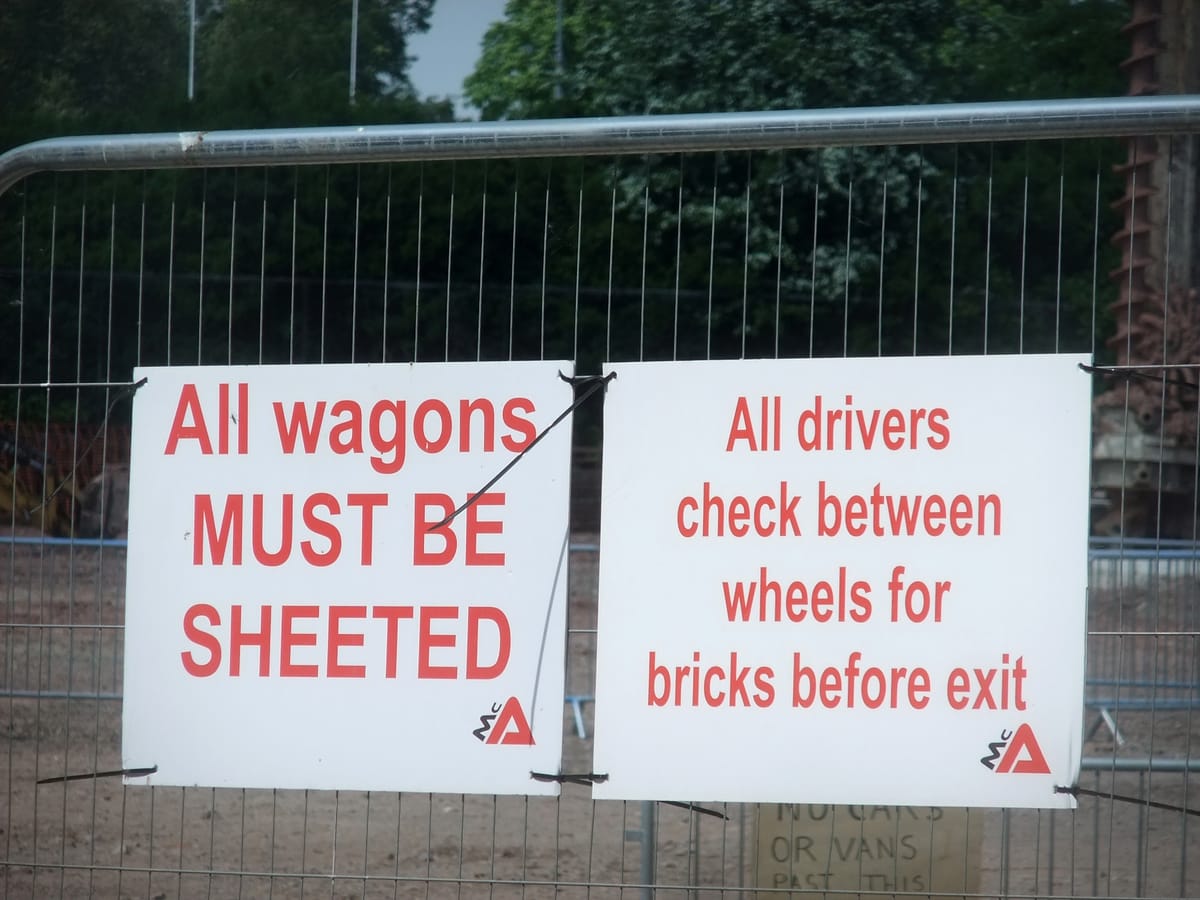 A sign on a fence reading, "All wagons MUST BE SHEETED."